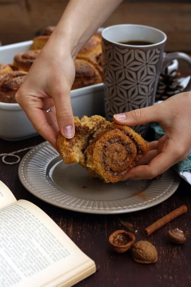 Healthy Cinnamon Sweet Potato Rolls - Breaking One Piece in Parts with a Book Next to the Plate