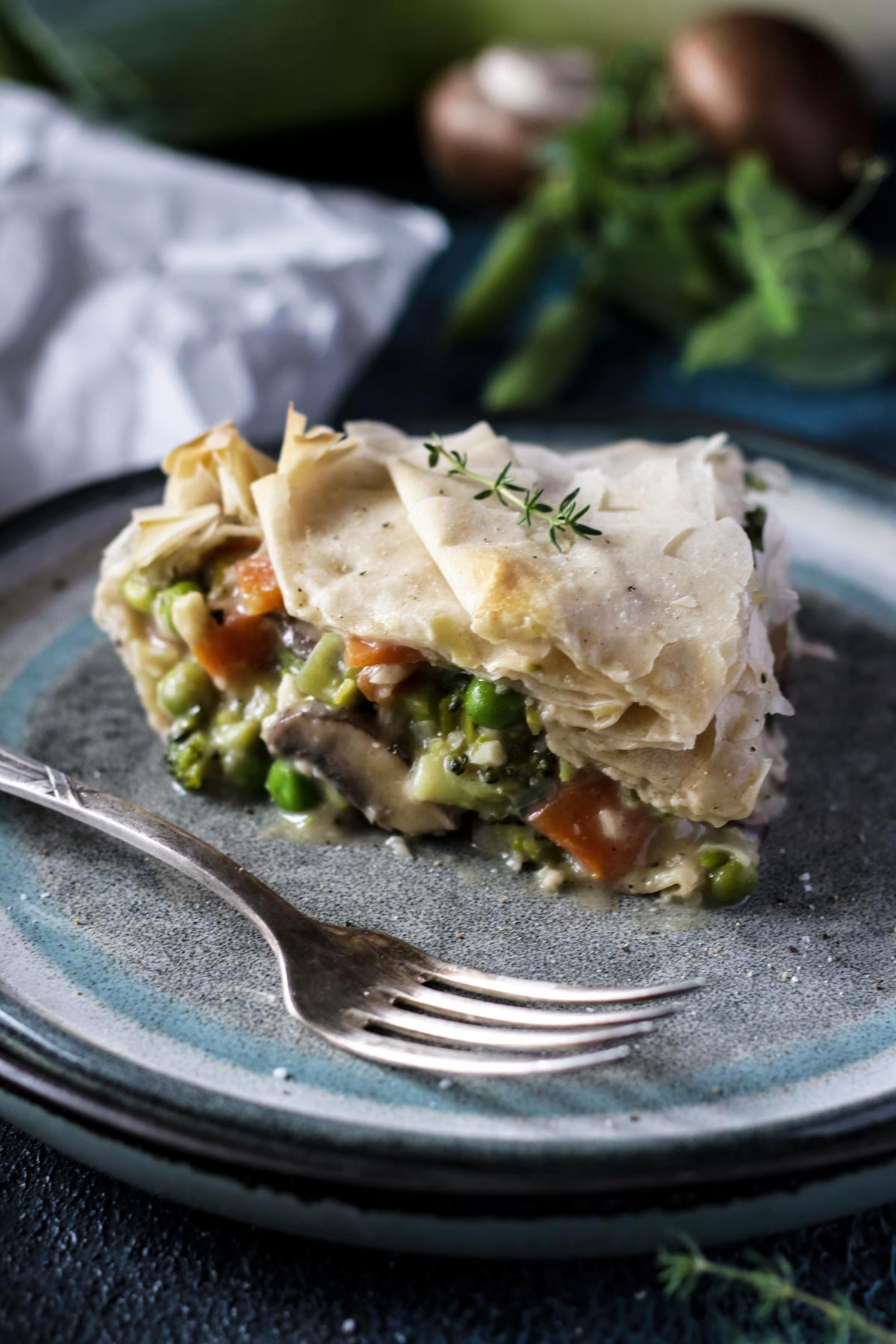 A Slice of Phyllo Pot Pie with vegetables and mushrooms on a grey plate with a fork.