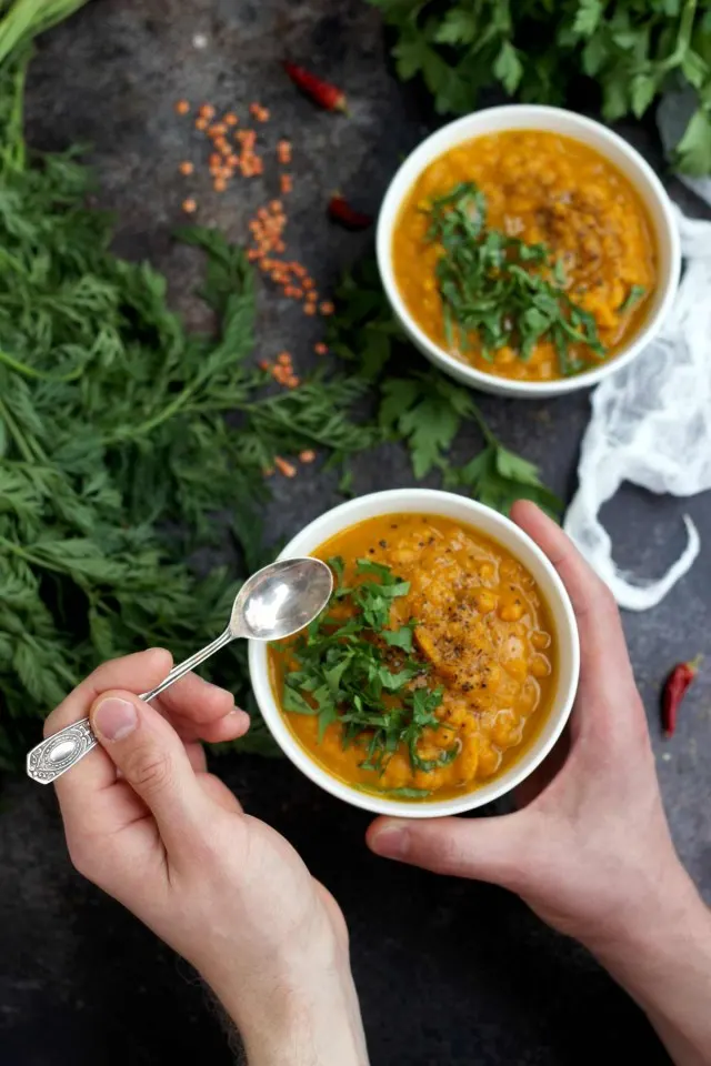 Vegan Roasted Carrot Soup with Lentils - Holding a Bowl with a Spoon Ready to Eat