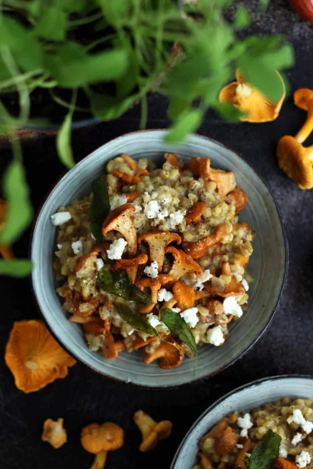 Easy Barley Risotto with Mushroom and Goat Cheese in a Bowl Flatlay with Greensin the Foreground and Raw Chanterelles Lying Around
