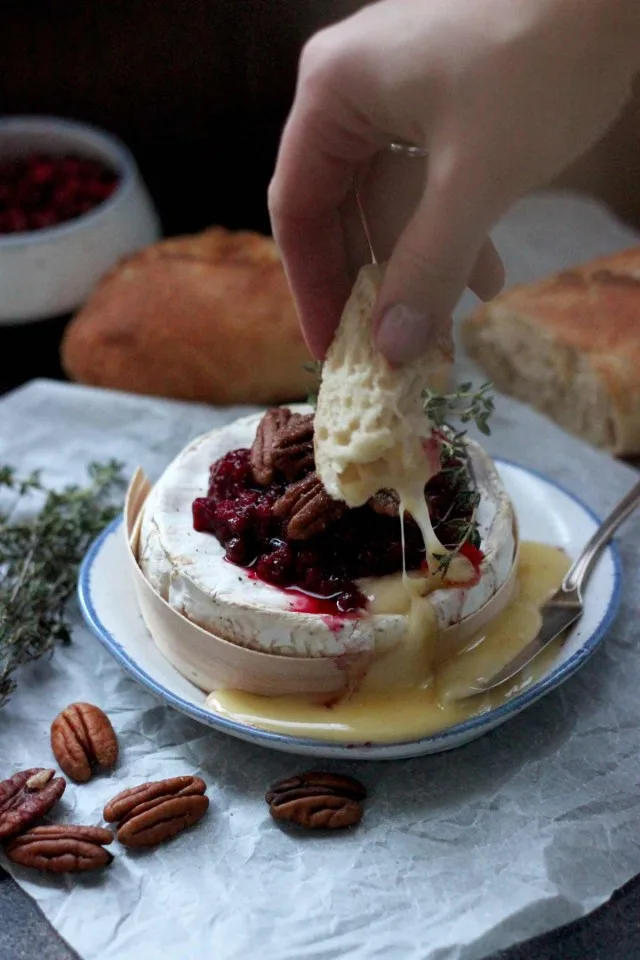 Easy Cranberry Baked Brie with Thyme Dipping a Piece of Bread