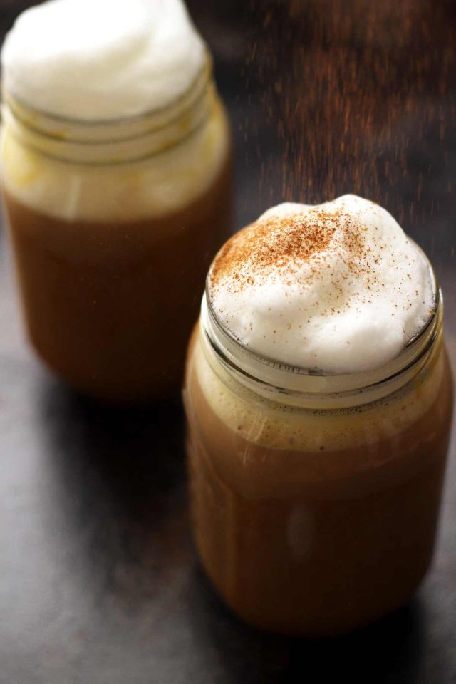 Healthy Vegan Pumpkin Spice Latte in a Mason Jar Topped with Cashew Whipped Milk Being Sprinkled with Cinnamon