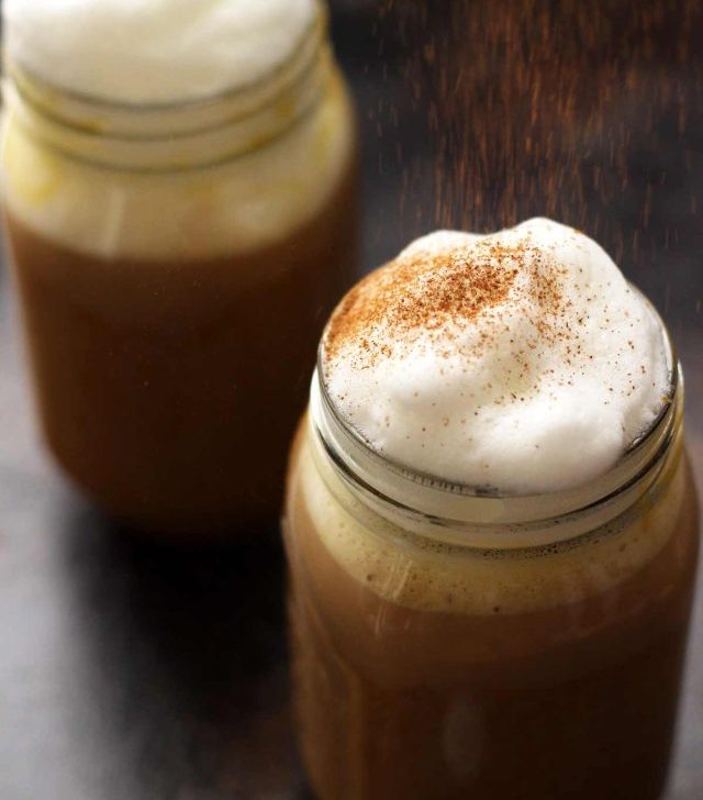 Healthy Vegan Pumpkin Spice Latte in a Mason Jar Topped with Cashew Whipped Milk Being Sprinkled with Cinnamon