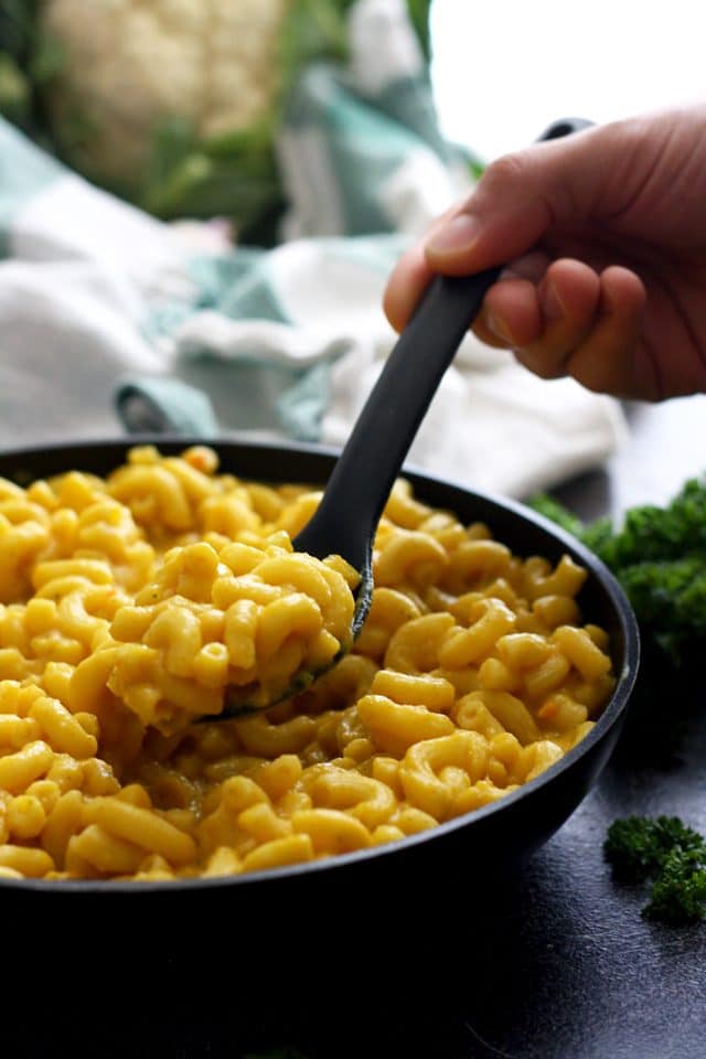 Silky Vegan Mac and Cheese - Serving with a Black Spoon with Herbs Around the Pan