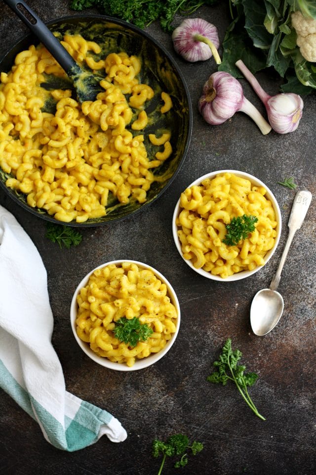 Silky Vegan Mac and Cheese Overhead Shot on Two Bowls and a Pan with Garlic and Herbs Around