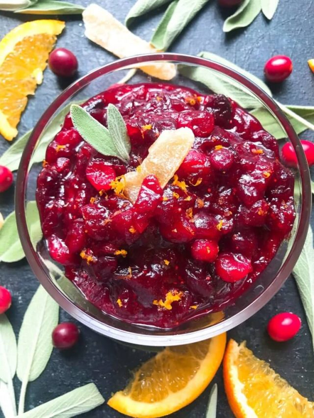 Ginger Orange Cranberry Sauce garnished with sage surrounded by oranges, cranberries and sage leaves.
