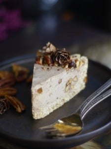 Pecan pie cheesecake decorated with pine cones on a dark plate.