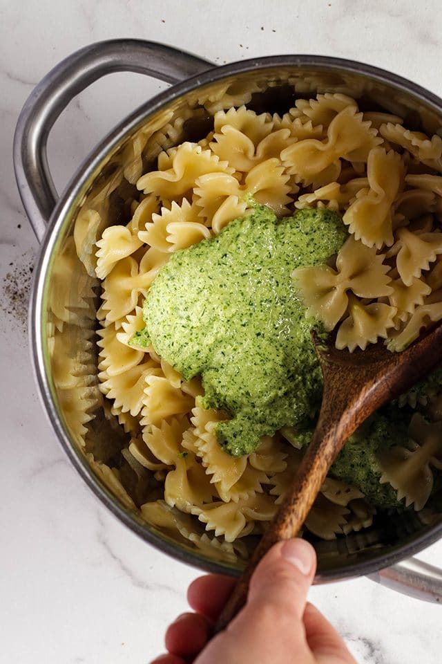 Farfalle pasta and vegan pesto in a pot being stirred with a wooden spoon