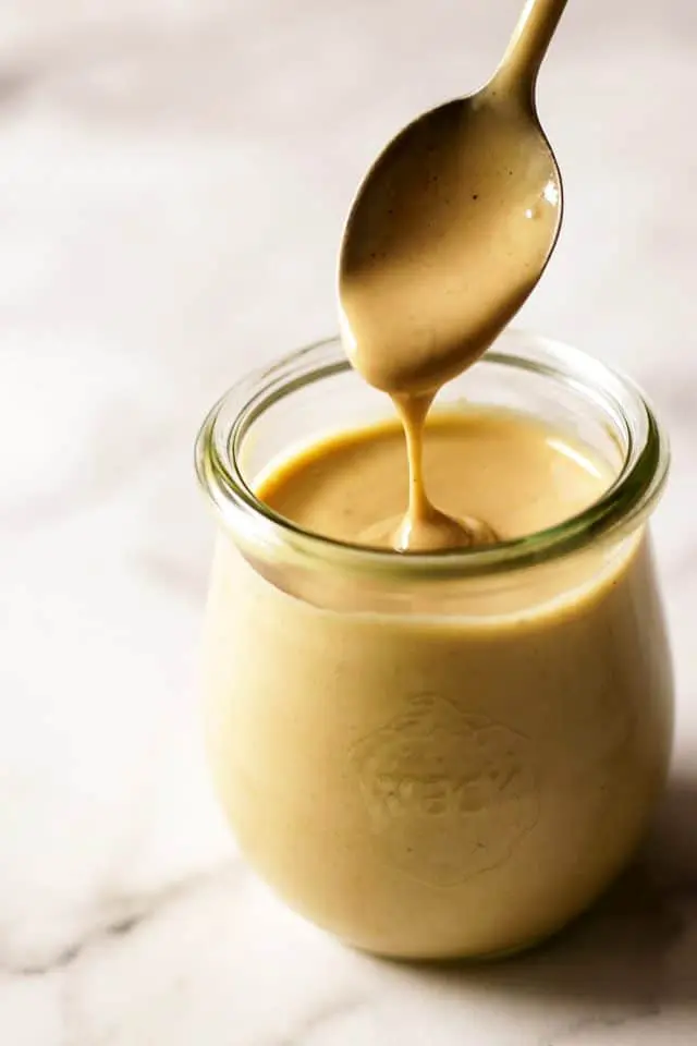 Tahini Dressing Dripping from a Spoon into a Jar