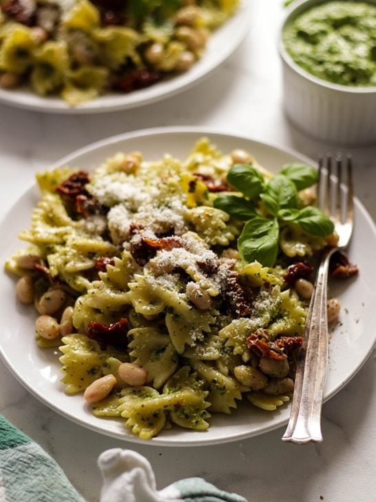Vegan pesto pasta on a plate next to a bowl of pesto and a cloth napkin