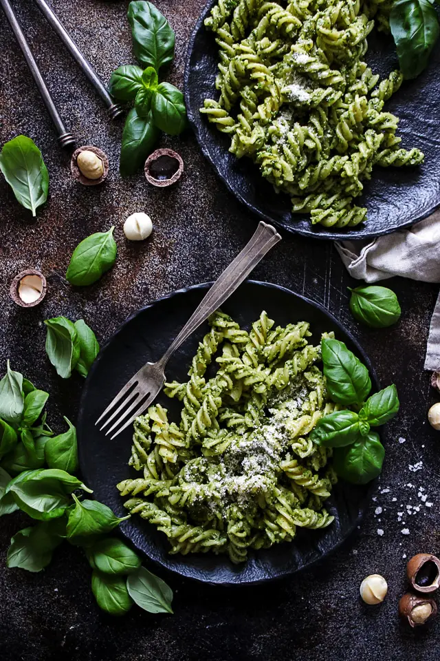 The Bowl of Vegan Pesto Pasta Garnished With Basil Leaves and Chopped Macadamia Nuts
