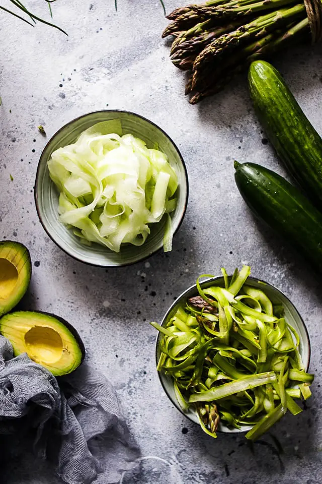 Shaved Asparagus and Shaved Cucumber in Bowls next to Asparagus, Avocados and Cucumbers