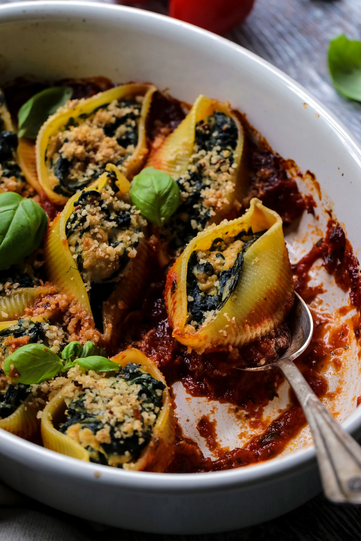Vegan stuffed shells on a baking dish with a serving spoon.