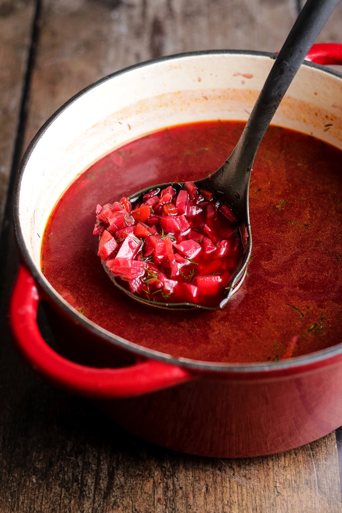 A ladle of vegan borscht in a large red pot.