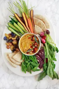 Pumpkin hummus surrounded by vegetables on a platter.