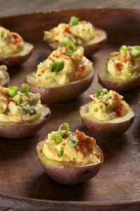 Vegan devilled eggs garnished with scallions on a wooden plate.
