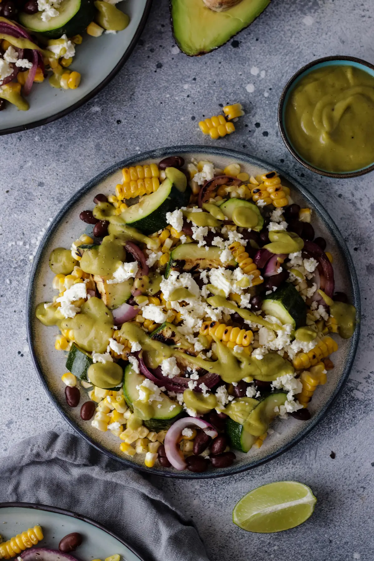 A Plate with Grilled Corn and Black Bean Salad Next to a Bowl with Avocado Dressing