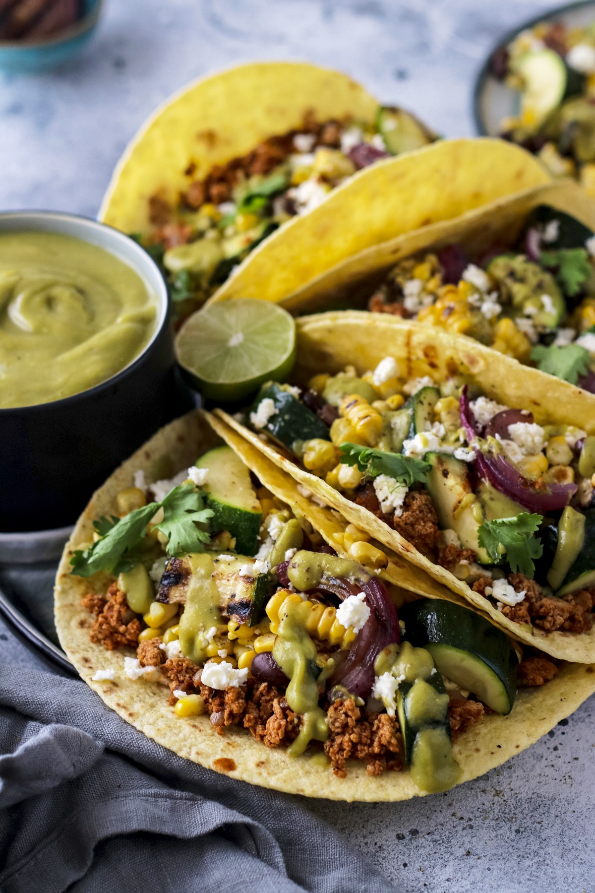 Vegetarian tacos on a plate next to avocado sauce.