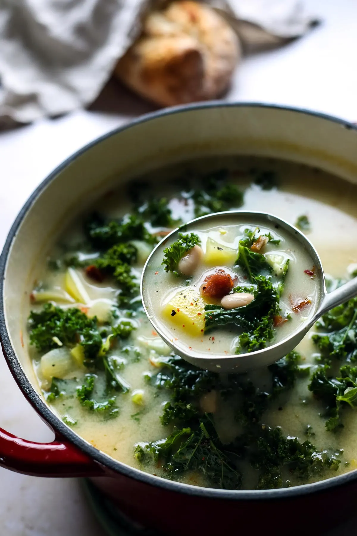 A ladle of vegan zuppa Toscana with kale and potatoes.
