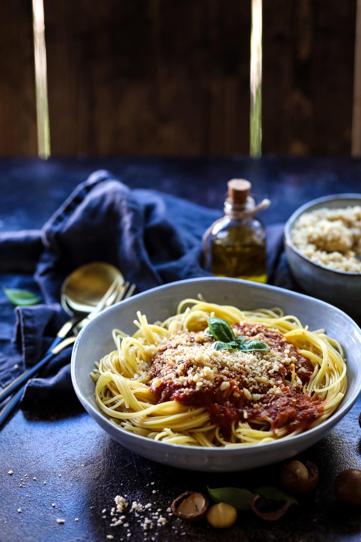 Spaghetti with Tomato Sauce and Vegan Parmesan Next to a Bottle of Olive Oil.