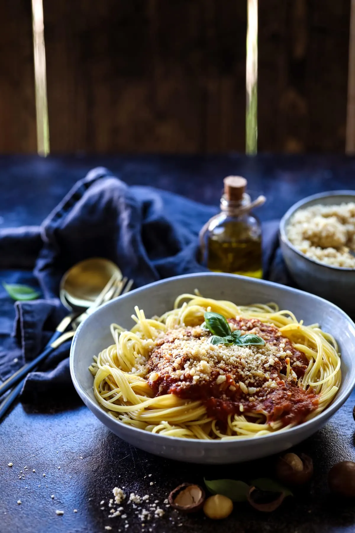 Spaghetti with Tomato Sauce and Vegan Parmesan Next to a Bottle of Olive Oil.