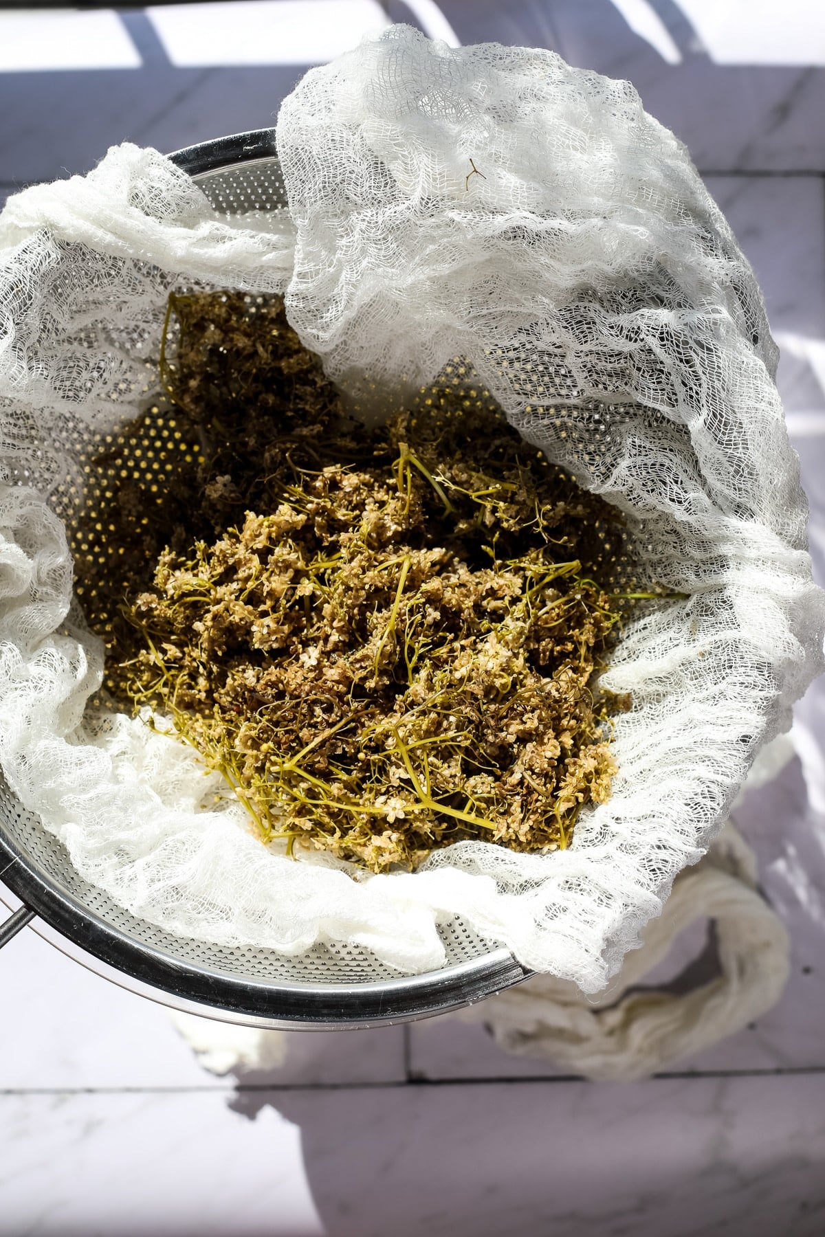 Straining elderflower syrup through cheesecloth.