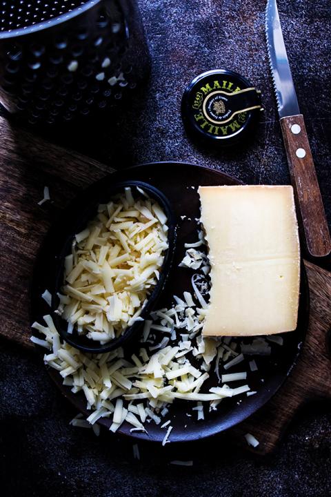 Grated Gruyere Cheese for Asparagus Quiche next to a Grater and a Knife